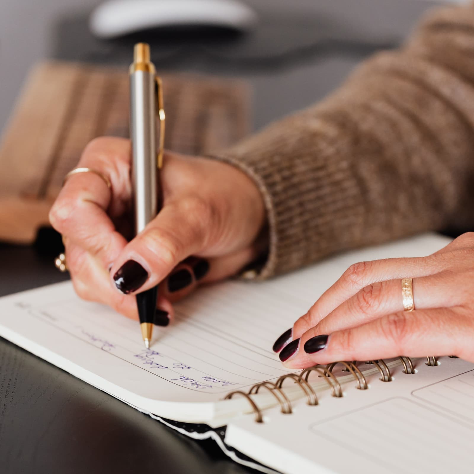 Hands writing with a pen in a spiral-bound notebook.